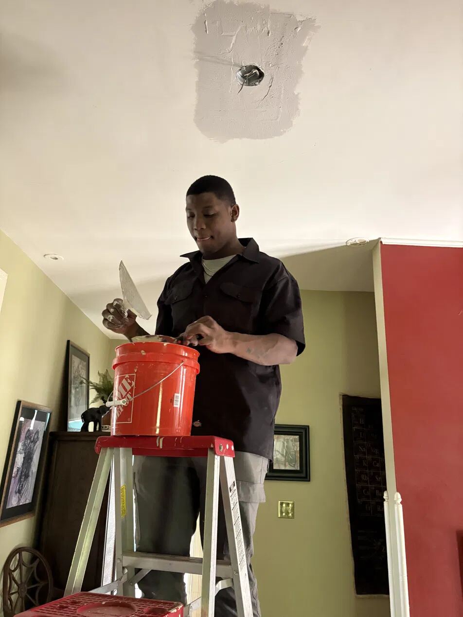 Stringer founder repairing a ceiling on a ladder in a client's home.